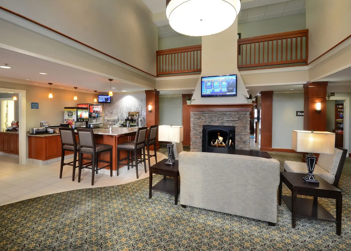 A cozy common area interior with a fireplace, bar area, comfortable seating, and a wall-mounted TV. The space invites guests to relax, socialize, or enjoy refreshments in a warm and friendly atmosphere.