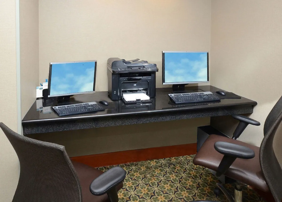 A dedicated workspace setup with two computer monitors, printer, sleek black desk surface, and ergonomic chairs. The environment is tailored for productivity, remote work, and seamless connectivity.