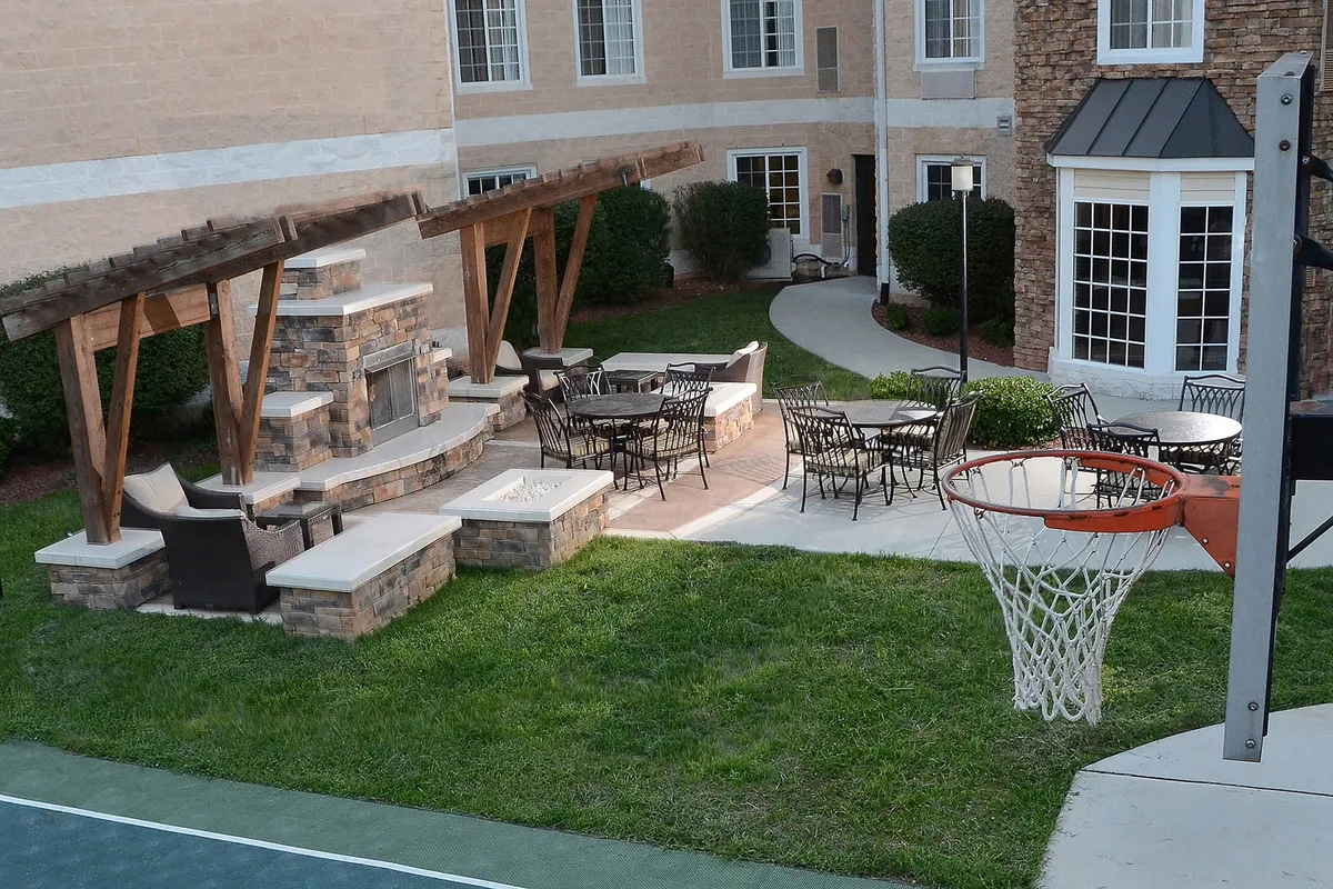 An exterior shot featuring a vibrant outdoor seating area, a cozy fireplace, and a basketball hoop. The space is designed for both relaxation and recreation, blending social and active experiences.